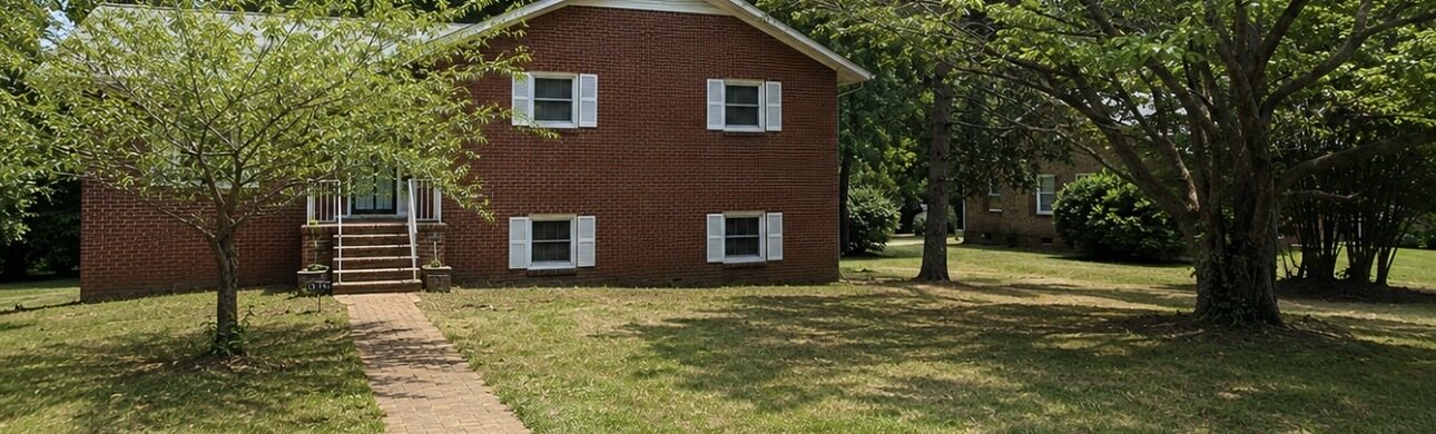 A brick house with the yard opened up and the ground clear around the mature trees